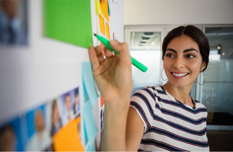 smiling-woman-writing-on-sticky-note-in-office-2021-08-28-17-22-39-utc 1